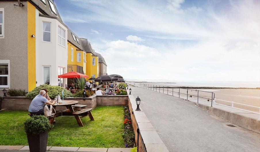 Guests dining on the Promenade Bistro Bar Terrace, looking out over the beach at The Beaches Hotel.