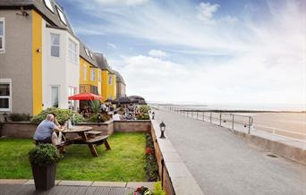 Guests dining on the Promenade Bistro Bar Terrace, looking out over the beach at The Beaches Hotel.