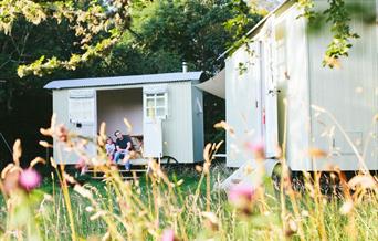 Father and son sitting in doorway of he shepherd's hut in a meadow of pink flowers